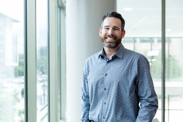 Standing in his office, the mature adult male entrepreneur smiles for his headshot.